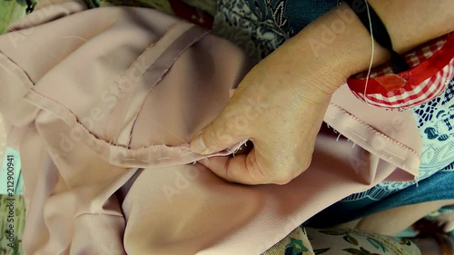 Older woman sewing by hand with needle, thread and thimble. Making a pink dress. seamstress working at home.
