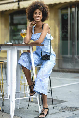 Portrait of fashionable young woman with camera drinking beer outdoors