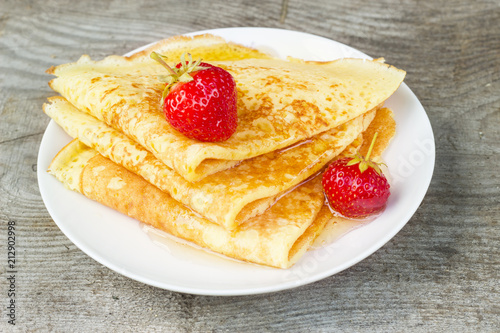 Tasty sweet thin pancakes with fresh strawberries and honey on plate  delicious dessert  closeup  wooden background