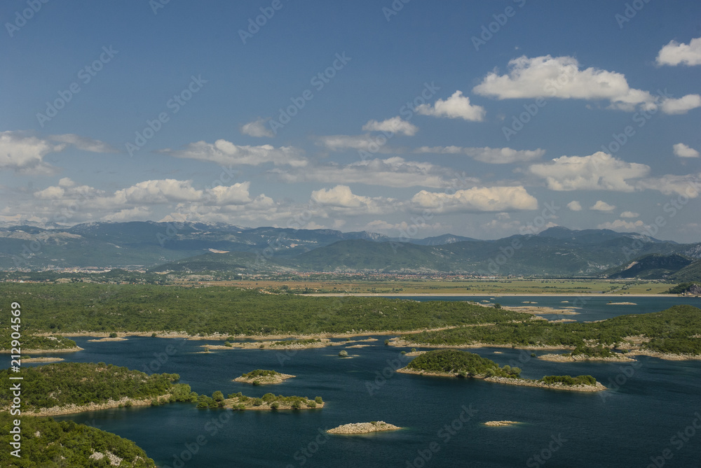 Earth patches and clouds/Landscape image with a lake having small islands and the cloud patches in the sky with mountains in the background.