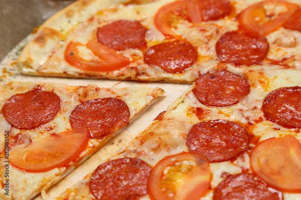 Pizza thin with smoked sausage, cheese, spices and tomatoes on a wooden stand. Cherry tomatoes and sweet peppers, lettuce leaves. Close-up Pizza thin with smoked sausage, cheese, spices and tomatoes on a wooden stand. Cherry tomatoes and sweet peppers, lettuce leaves. Close-up