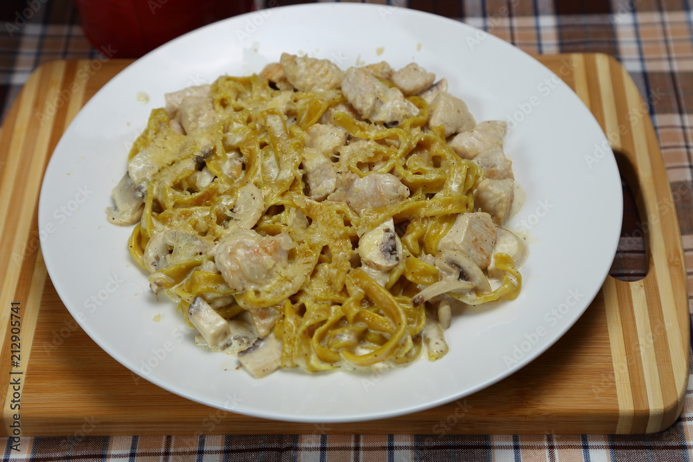 Macaroni with chicken meat and mushrooms. Spice. Red metal glass with a spoon, fork and knife.