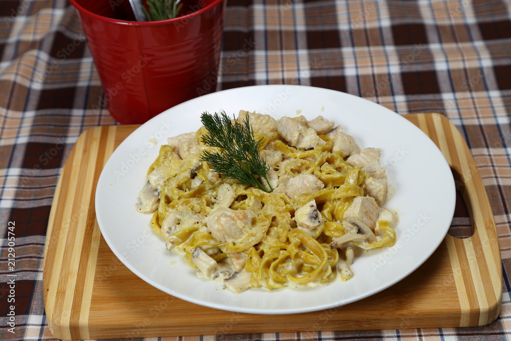 Macaroni with chicken meat and mushrooms. Spice. Red metal glass with a spoon, fork and knife.