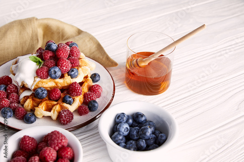 delicious belgian waffles with berries and honey on white wooden table