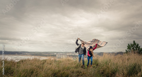 Portrait of young beautiful couple playing outdoors with blanket in a windy day over dark cloudy sky