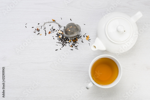 cup of tea with teapot and closed infuser with black tea on table photo