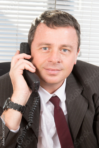 portrait of businessman smiling and speaking in phone at workplace