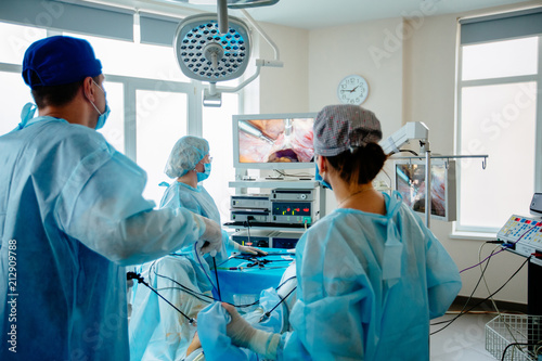 Back view of surgeons team looks at monitors while preforming operation in hospital operating theater, male surgeon operating patient working with surgical laparoscopy instruments. Gynecology. photo