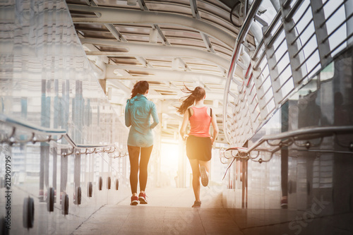 Two young woman runners sprinting outdoors - Sportive people training in a urban area, healthy lifestyle and sport concepts.
