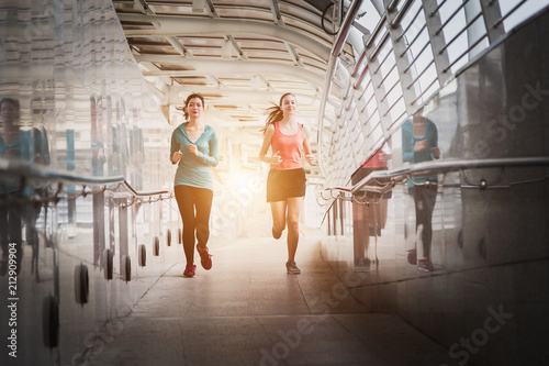Two young woman runners sprinting outdoors - Sportive people training in a urban area, healthy lifestyle and sport concepts.