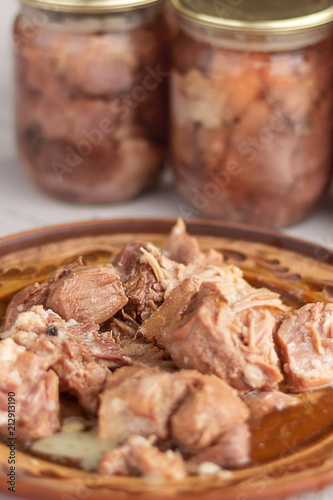 pieces of stew meat on a clay plate on the background of glass cans with home preservation. Home cooking
