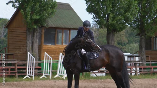 A young girl rider rides a horse on horseback sitting in the saddle and strokes the horse around the neck. Dressage training HD