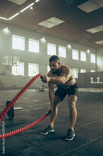 Fototapeta Naklejka Na Ścianę i Meble -  Men with battle rope battle ropes exercise in the fitness gym.
