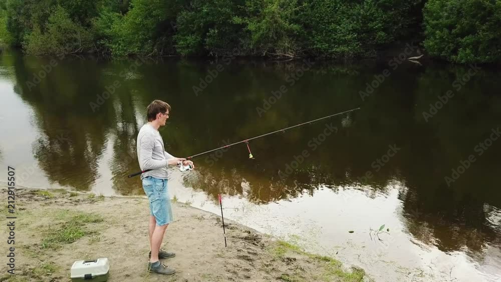 Fisherman with a fishing rod on the river bank. Man fisherman catches a fish. Concept of a rural getaway Fisherman with a fishing rod on the river bank. Man fisherman catches a fish. Concept of a rural getaway