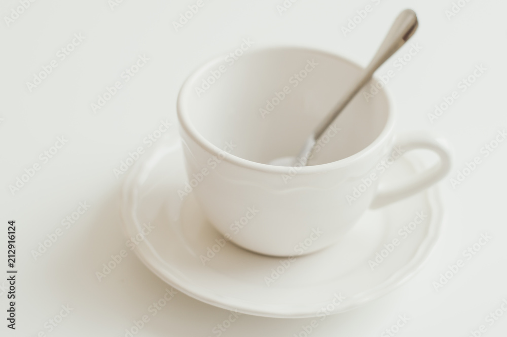 Empty cup of white color and small spoon on white table. Minimal style