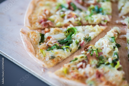 Original dünner Flammkuchen aus dem Elsass mit Zwiebeln, Speck und Sauerrahm Creme im Ofen gebacken uf einem Holzbrett serviert