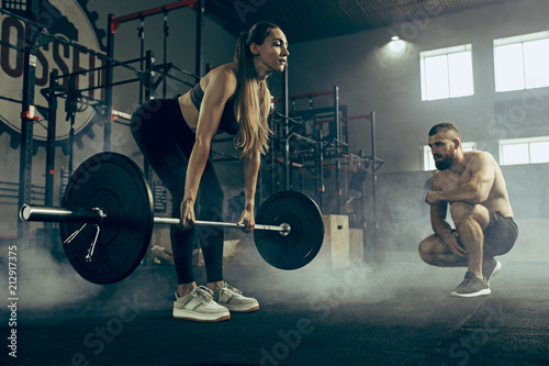 Fit young woman lifting barbells working out in a gym