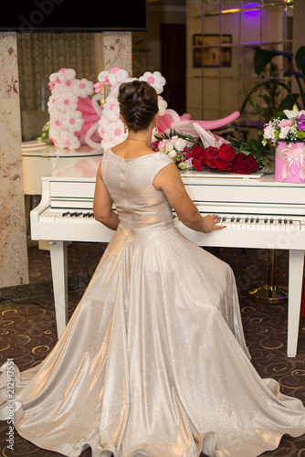Back view of woman in light dress sitting and playing piano. Concept of music and arts. flowers on the piano. photo