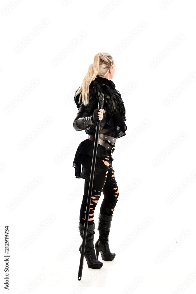 full length portrait of blonde girl wearing lack fantasy warrior outfit. standing pose wit bak to the camera. isolated on white studio background. full length portrait of blonde girl wearing lack fantasy warrior outfit. standing pose wit bak to the camera. isolated on white studio background.