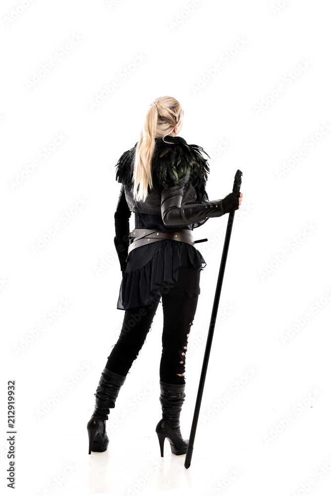 full length portrait of blonde girl wearing lack fantasy warrior outfit. standing pose wit bak to the camera. isolated on white studio background. full length portrait of blonde girl wearing lack fantasy warrior outfit. standing pose wit bak to the camera. isolated on white studio background.