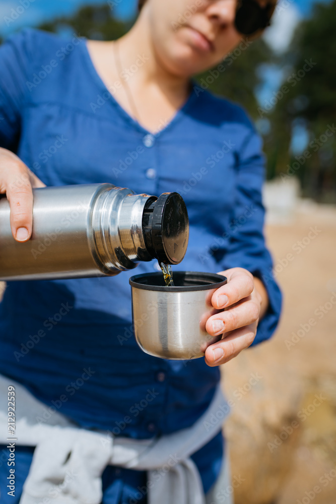 Naklejka premium Woman pouring hot tea from a thermos in the open air. On a sandy beach on a Sunny day. Close up.
