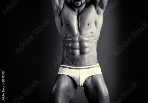 Penis concept. Close up of naked male body with perfect sic pack abs on dark background. Tense body of young man. Black and white photo of man's muscular body. Strip theme and adult entertainment.