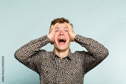 overjoyed extremely happy and excited man clutching his head. portrait of a young guy on light background. emotion facial expression. feelings and people reaction.