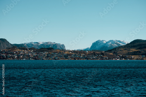 Beautiful scenic view of cold blue sea, island with small rorbu houses and mountains with snowy peaks on the background. Norway