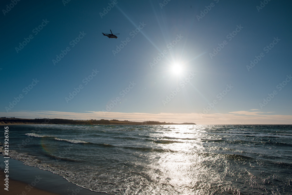 Helicopter flying over the sea with beautiful beach with yellow sand. Sunset. Norway