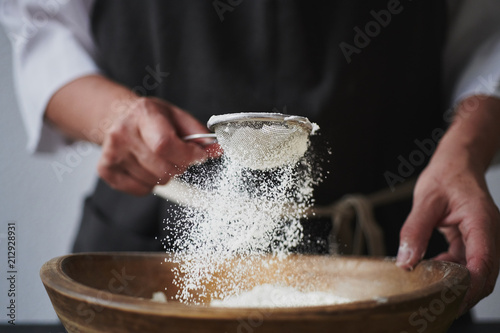 Slow motion shot of aged female hands sifting flour by sieve in wooden bowl. photo