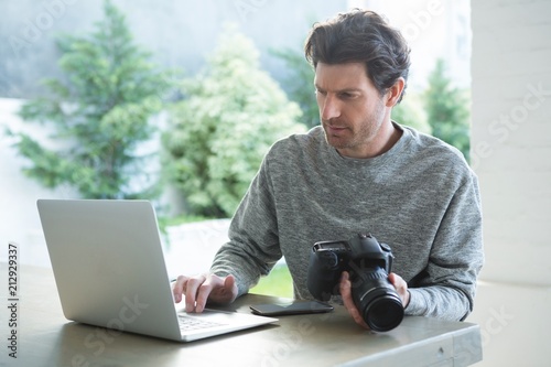 Man using laptop and holding digital camera photo