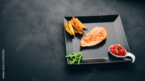 Baked chicken fillet with sesame seeds, potatoes and sauce. On a wooden background. Top view. Copy space.
