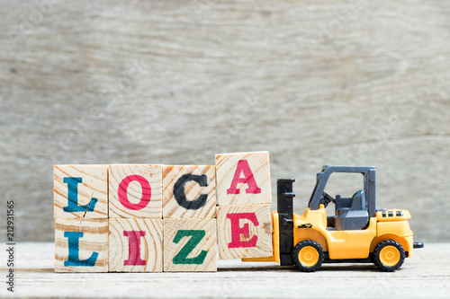 Toy forklift hold letter block a.e to complete word localize on wood background