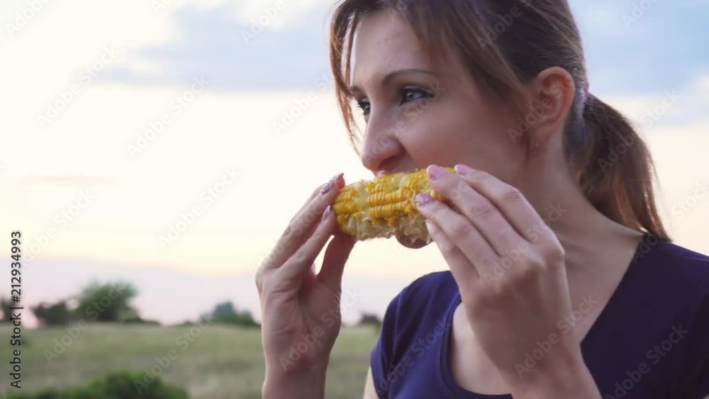 Young woman eating boiled corn at sunset