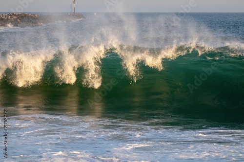 Large blue green wave crashing in the ocean during sunset