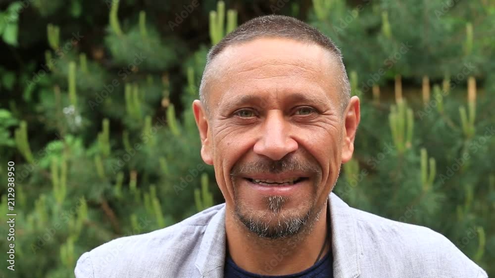 People and lifestyle concept. Happy middle-aged unshaven man with cheerful smile outdoor against green nature background. Adult man portrait close up People and lifestyle concept. Happy middle-aged unshaven man with cheerful smile outdoor against green nature background. Adult man portrait close up