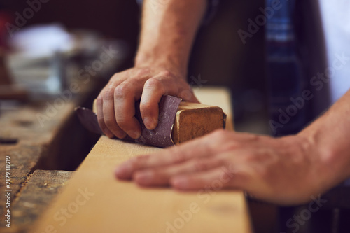 Close-up of carpenter using sandpaper on a wooden plank in a carpentry shop photo