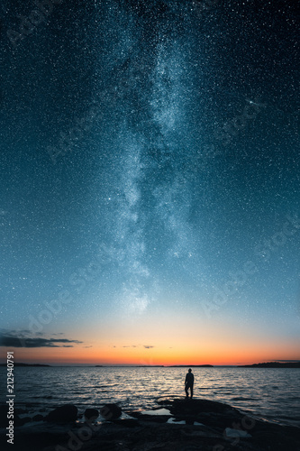 Fototapeta Naklejka Na Ścianę i Meble -  Silhouette of a man looking up on stars of the milky way with last light of sunset glows on the horizon