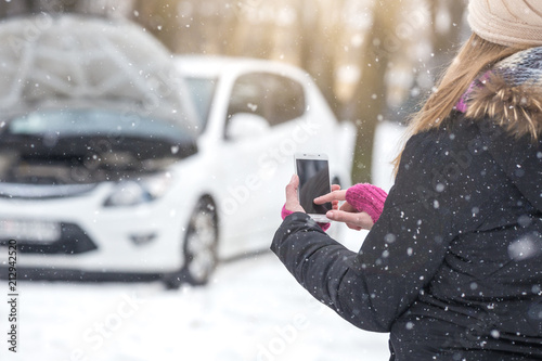 Female standing next to broken car and using mobile assistance smart phone app.