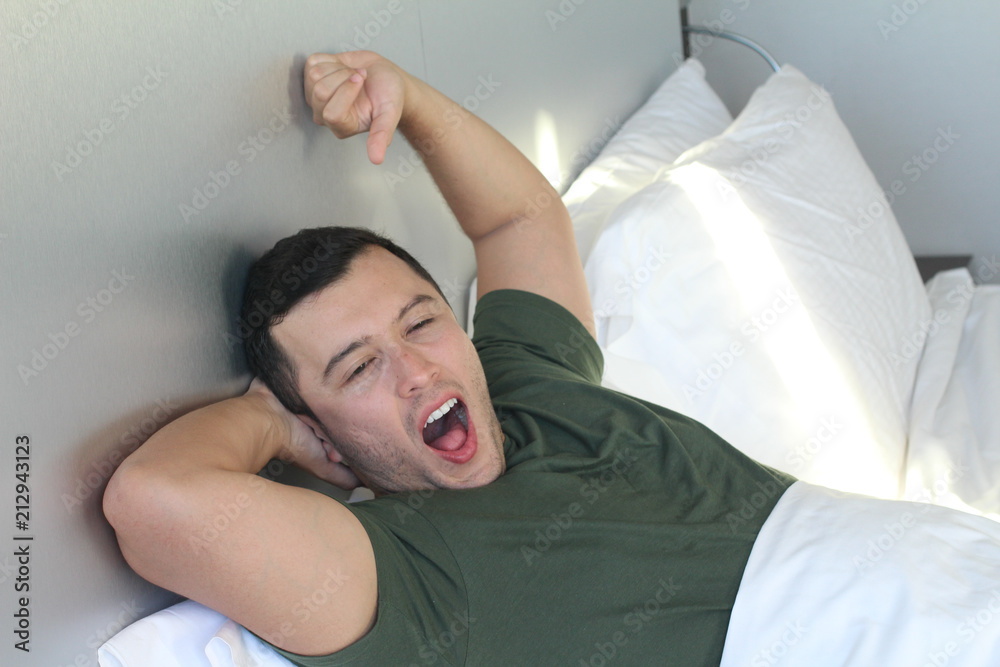 Young male yawning in bed 