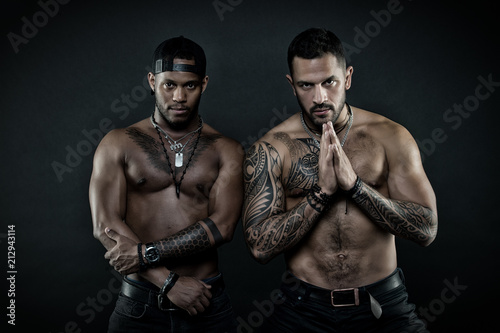 Sportsmen with sexy fit torsos. Martial arts contestants calming down before fight. Bodybuilders isolated on black background. Hispanic man with geometrical tattoos holding hands in prayer gesture