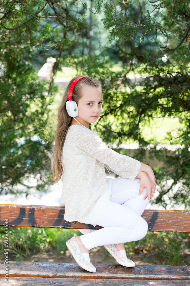 Naklejka premium Music sound and mp3. Little girl listen music in summer park. Child enjoy music in headphones outdoor. Fashion kid and modern technology. Summer vacation and fun