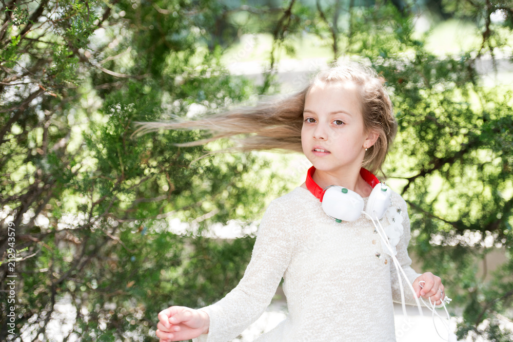 Small child enjoy music in headphones outdoor. Girl dance to music in summer park. Kid dancer with long flying hair. Melody sound and mp3. Summer fun and joy Small child enjoy music in headphones outdoor. Girl dance to music in summer park. Kid dancer with long flying hair. Melody sound and mp3. Summer fun and joy