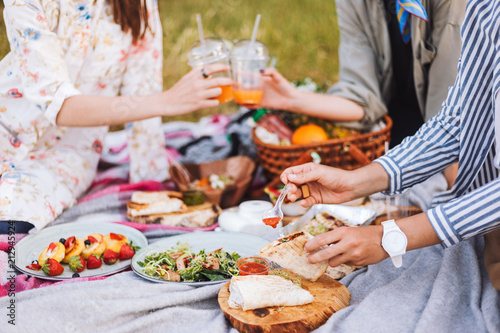 Close up girls spending time on beautiful picnic with variety of tasty food and drinks on picnic blanket in city park