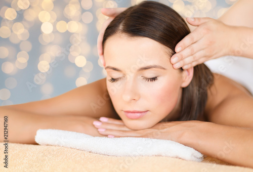 wellness, spa and beauty concept - close up of beautiful woman having head massage over holidays lights background