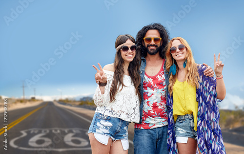 nature, summer, youth culture, gesture and people concept - smiling young hippie friends in sunglasses showing peace hand sign over us route 66 background
