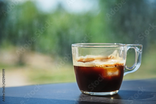 Transparent glass cup of ice coffee placed on a dark wooden laminated table surface