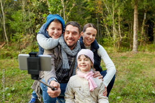 family and technology concept - happy mother, father, son and daughter taking picture by smartphone on selfie stick outdoors © Syda Productions