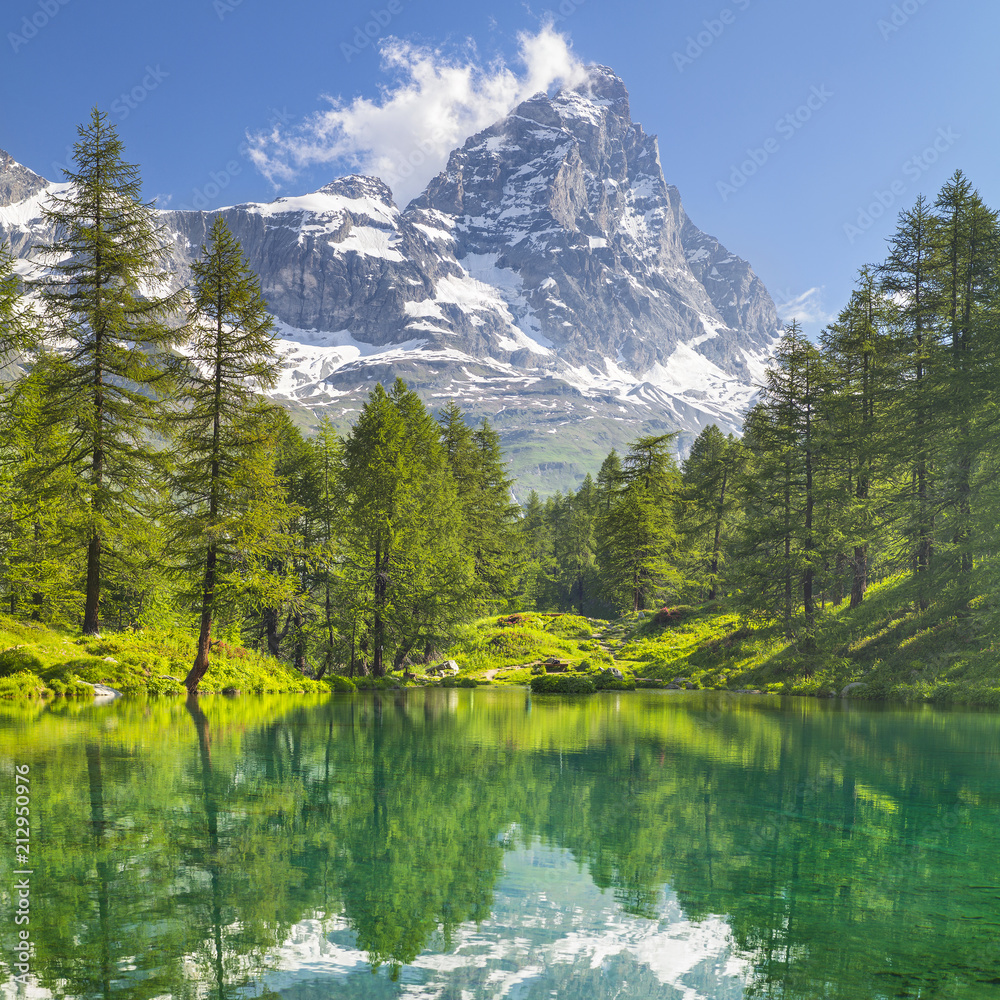 view to mountain peak Matterhorn and forest lake with emerald water and pines in Italy