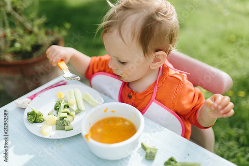 Portrait of adorable baby girl eating puree sitting at baby table outdoor